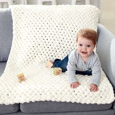 a baby laying on top of a gray couch next to a white blanket and wooden blocks