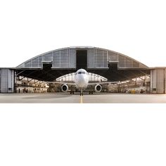 an airplane is parked in front of a hangar with its doors open on the tarmac