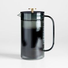 a black glass coffee pot with a gold top on a white surface, in front of a plain background