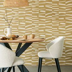 a dining table with two chairs and a vase on it, in front of a patterned wall