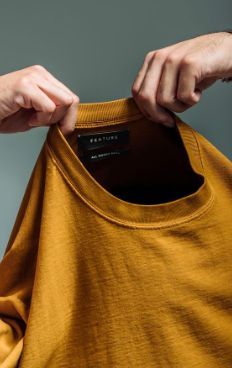 a person holding onto an orange t - shirt with their hands on the hanger