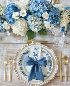 a blue and white table setting with silverware, flowers and napkins on it