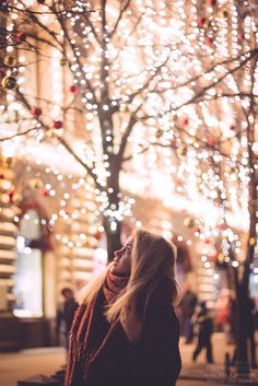 a woman standing in front of a tree with lights on it