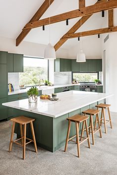 a large kitchen with green cabinets and white counter tops, along with wooden stools