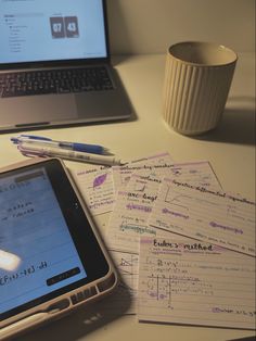 a laptop computer sitting on top of a desk next to a pile of paper with writing on it