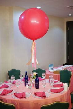 a round table with pink linens, green chairs and a large red balloon hanging from the ceiling