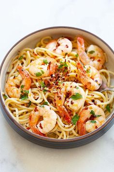 a bowl filled with pasta and shrimp on top of a white countertop next to a fork