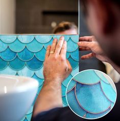 a man is painting a tile with blue scales on the wall next to a sink