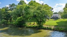 a river running through a lush green forest next to a large white house on top of a hill