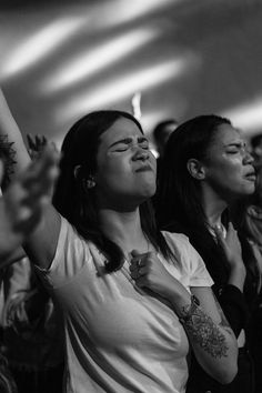 two women are standing in the audience and clapping with their hands up while one woman is holding her cell phone