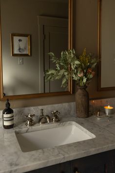 a white sink sitting under a bathroom mirror next to a vase with flowers on it