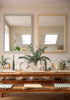 a wooden table topped with plates and vases filled with plants next to two mirrors