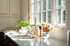 a kitchen with white cabinets and gold faucets on the counter top, next to a window