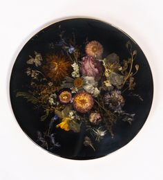 a black plate with flowers on it sitting on a white table top next to a wall