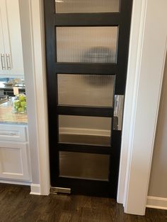 a black door in a white kitchen with wood flooring and glass panels on the doors