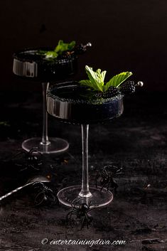 two martinis with green leaves in them on a dark surface, ready to be served