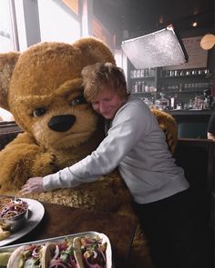 a woman hugging a giant teddy bear at a restaurant table with food on the side