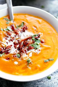 a white bowl filled with carrot soup topped with bacon and parmesan flakes