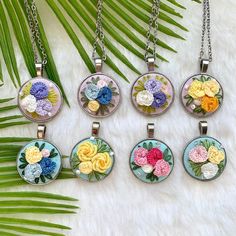 six necklaces with flowers on them sitting next to palm leaves