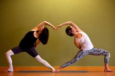 two women doing yoga poses in the middle of a room with green walls and wood flooring