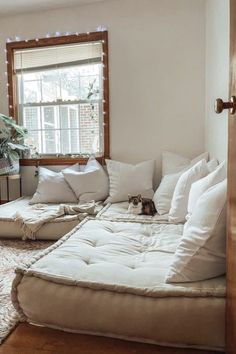 a living room filled with lots of white furniture and pillows on top of a wooden floor