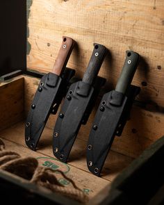 three knives are in a wooden box on the floor and one is black with brown handles