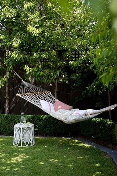 a hammock hanging in the middle of a yard next to a small table