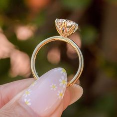 a hand holding a yellow gold ring with flowers on the band and a diamond in the middle