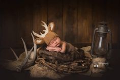 a newborn baby wearing a deer hat is posed in a nest with antlers and other items