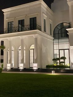 a large white house lit up at night with lights on the windows and balconies