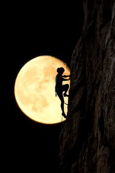 a man climbing up the side of a mountain with a full moon in the background