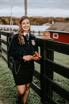 a young woman standing next to a fence holding an item in her hand and smiling at the camera