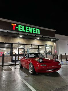 a red sports car is parked in front of a 7 eleven store at night time