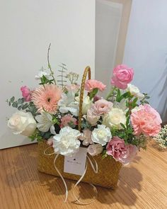 a basket filled with pink and white flowers on top of a wooden table next to a wall