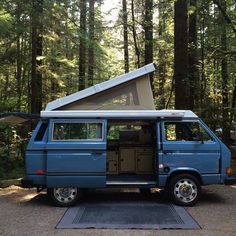 a blue van parked in the middle of a forest with a tent on it's roof