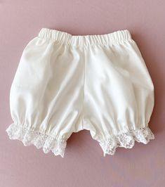 a pair of white shorts with lace trims on the bottom and side, against a pink background