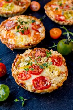 small pizzas with tomatoes, cheese and herbs on a table next to green peppers