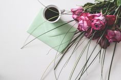 a bouquet of pink flowers next to a cup of coffee on a white table top