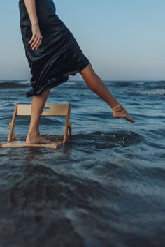 a woman standing on top of a chair in the middle of the ocean with her legs spread out