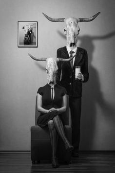 a man and woman sitting on a chair with long horns over their heads in front of them