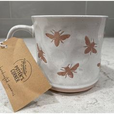 a white coffee cup with brown bees on it and a tag hanging from the handle