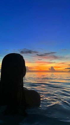 a woman sitting in the water at sunset with her back to the camera, looking out into the distance