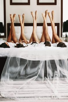 four women laying on top of a bed with white sheets and veils covering them