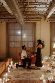 a man kneeling down next to a woman in a living room filled with lit candles