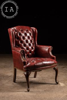 a red leather chair sitting on top of a cement floor next to a black wall