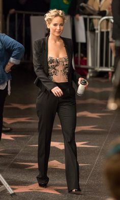 a woman in a black suit is holding a drink and looking at the camera with an instagramr