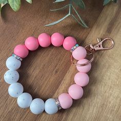 a pink and white beaded bracelet on a wooden table next to a potted plant