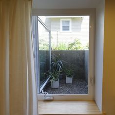 an open window in a small room with plants on the windowsill and a house behind it