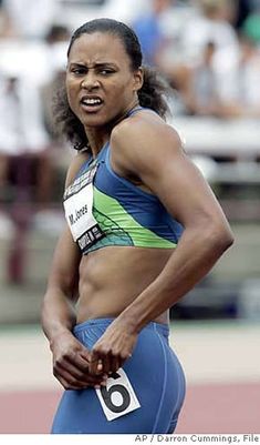 a woman in a blue and green sports bra standing on a track with her hands behind her back