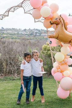 two young children standing under a balloon arch